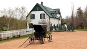 A horse drawn carriage buggy parked on an unpaved road near a building