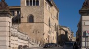 A street with parked cars runs by old buildings with Renaissance architecture