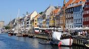 Sailboats docked alongside a bustling waterfront lined with gabled buildings and cafes