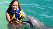A girl poses, smiling, with a dolphin