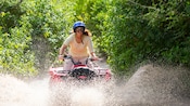 A woman splashes through a mud puddle on an ATV