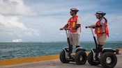 Un hombre y una mujer montando Segways mirando al océano y los cruceros atracados a la distancia