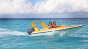 2 Guests in life jackets smile as they speed through the water in a mini speedboat