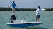 Man stands on bow of a small boat with a fly fishing rod and reel