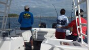 Two tour guides watch on as a Guest fishes off the side of a troll boat