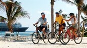 Tres visitantes andan en bicicletas por una ruta en el mar