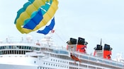 A couple tandem parasails next to a Disney Cruise Line ship