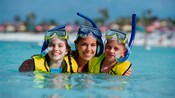 3 young girls in snorkel gear smile as they stand in the ocean