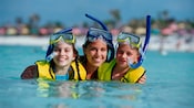 3 young girls in snorkel gear smile as they stand in the ocean