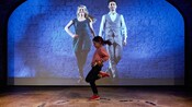 A girl dances in front of a wall with a projection of 2 river dancers