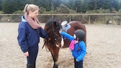 A young girl pets a pony wearing a saddle and bridle
