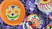 A decorative skull cookie next to 2 decorative skulls