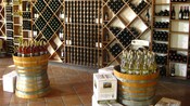 A tasting room with wine bottles stacked in wine racks and arranged on top of wine barrels