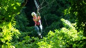Front view of smiling girl in a helmet zip lining through forest