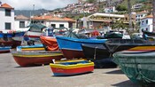 Bows of ships of different sizes sitting on concrete in front of a hillside covered with houses