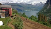 A tractor sitting on a dirt hillside with a lake and mountains in the background