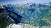 A parking area overlooking a valley, a fjord and a mountain range