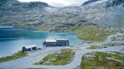 A building sits in front of a lake and gravelly hillside with sparse vegetation