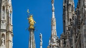 A statue of a haloed figure atop a spire near ornate spires