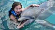 A little girl poses for a picture, hugging a dolphin