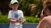 A young boy smiles as he holds a sea turtle and poses for the camera