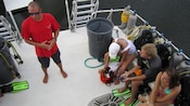 Three young adults on the back of a boat receive instructions from an instructor as they prepare to scuba dive