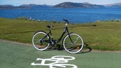 Uma bicicleta em uma ciclovia próxima da água com colinas ao longe