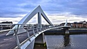 A metal pedestrian bridge with an s curved span stretching over a waterway