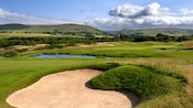 A golf course fairway with a sand trap and a water hazard beyond it