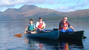 2 men in a canoe floating next to a woman in a canoe