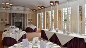 Interior of a dining room featuring windows and set tables with linens, menus and floral centerpieces