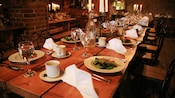 A restaurant dining room with wooden tables and lit candles, surrounded by brick walls