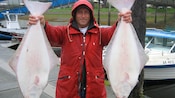 Um homem nas docas e segura um peixe halibute em cada mão