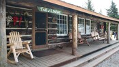 Wooden rocking chairs and benches sit on the porch of a large log building