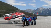 Um grupo de pessoas lado a lado em frente a um helicóptero no topo de uma geleira