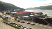 Uma construção grande de um andar na costa de uma baía cercada por colinas cobertas por árvores