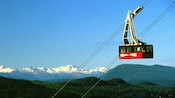 Un teleférico suspendido en el aire en un entorno de colinas ondulantes y cumbres nevadas a la distancia