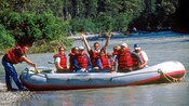 A man with both arms outstretched sits among a group of people in an inflatable raft