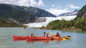 People kayaking by Mendenhall Glacier surrounded by mountains with greenery