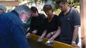 A group of people stand at a trough holding small pans filled with silt and water