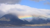 Clouds trapped between the valleys of a mountain range create a rainbow above the town below