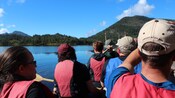 A small group paddling through the calm waters toward forested mountain terrain