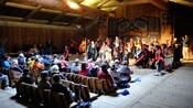An audience watches a show featuring multiple characters in elaborate costumes