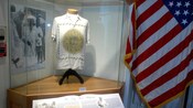 Museum exhibit of a shirt with the Mayan calendar printed on it and an American flag hanging next to it