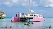 Um catamarã atracado em uma enseada rasa enquanto as pessoas mergulham com snorkel na água próxima enquanto outras ficam no convés