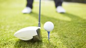 A golf club poised behind a ball on a tee as a golfer prepares to tee off