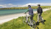 Two bicycle riders stopped on a grassy coastline taking in the view