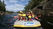 Una balsa que transporta a cuatro niños, cinco adultos y un guía por las aguas rápidas con un bosque denso de fondo