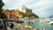 A castle and an ancient seaside village sit alongside a bay filled with boats