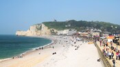 A beach dotted with people and cliffs at the far end